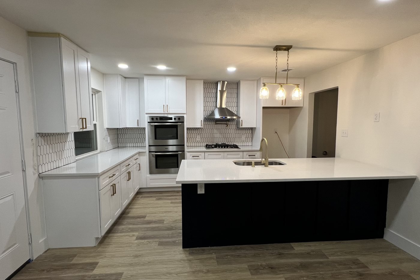 Remodeled kitchen with white cabinets, black island, stainless range hood and pendant lighting