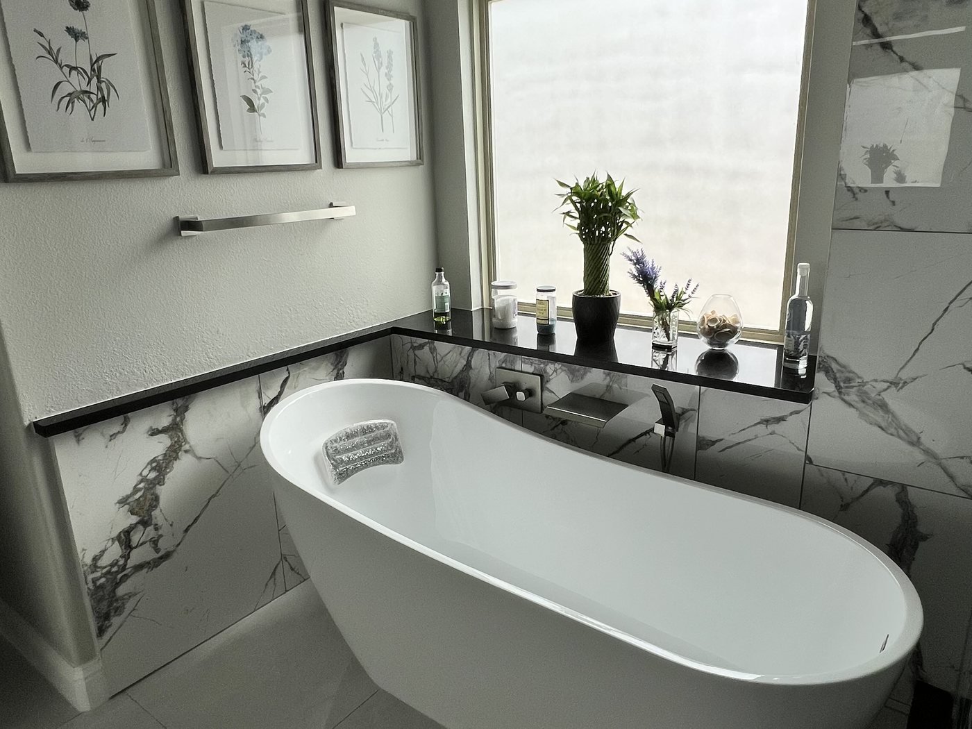 Primary bathroom with freestanding soaking tub, marble walls and framed botanical prints