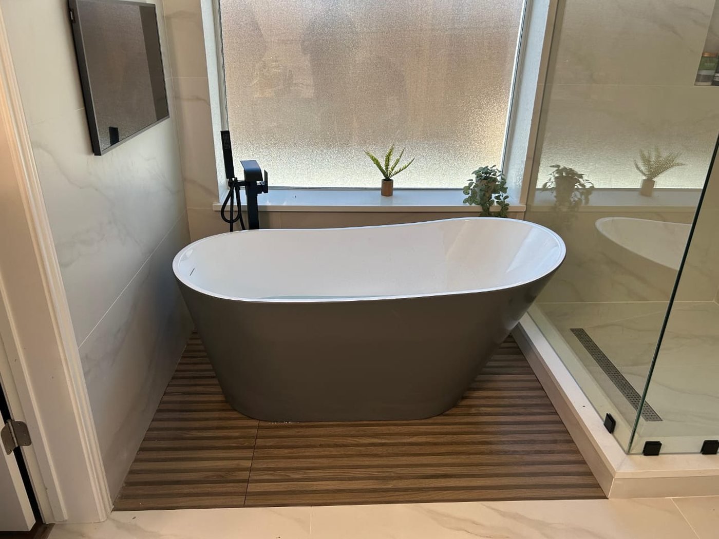 Master bathroom with freestanding tub on a wood-plank deck and black fixtures