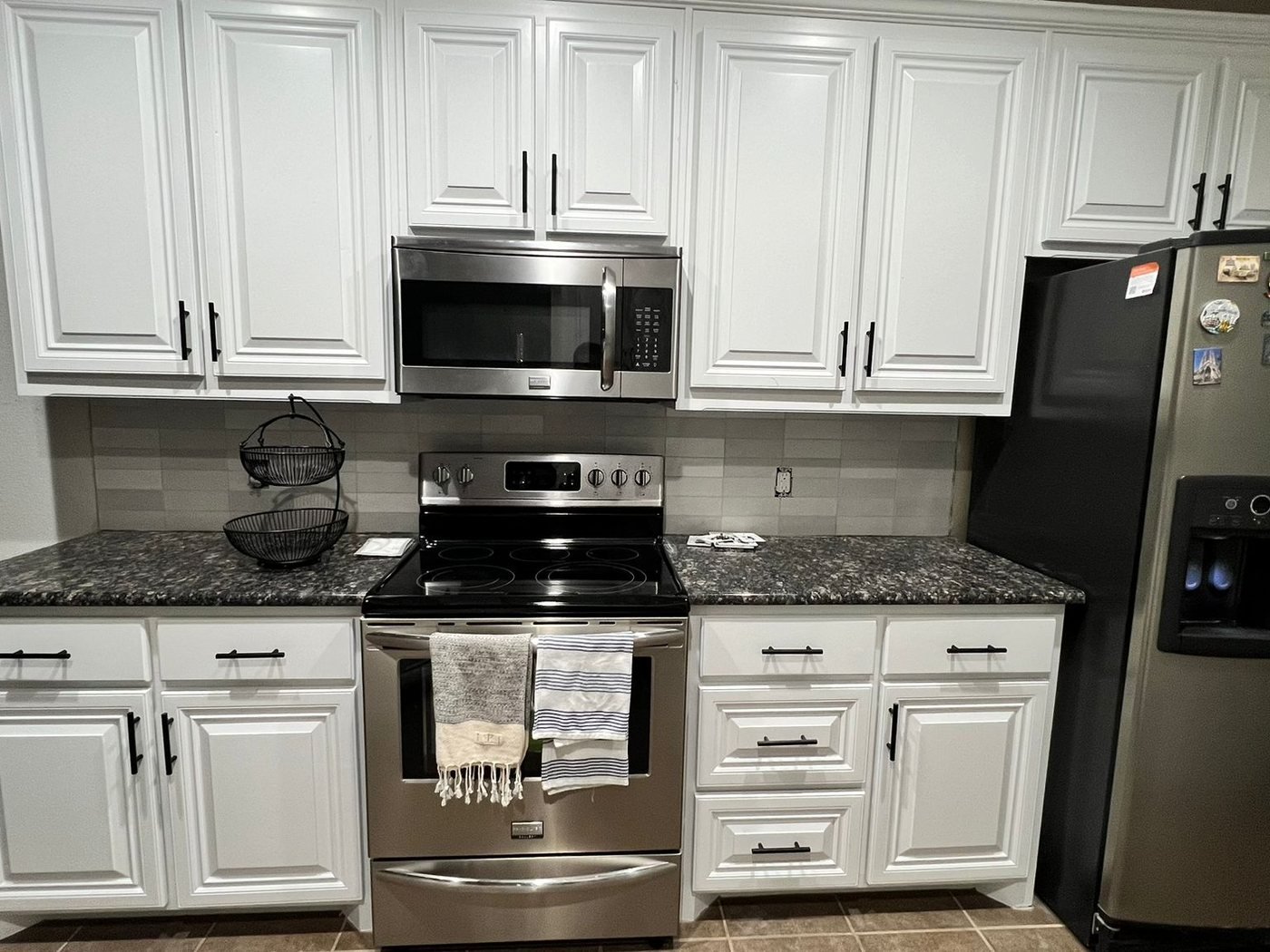 Kitchen cabinets refinished in white with black hardware and stainless appliances