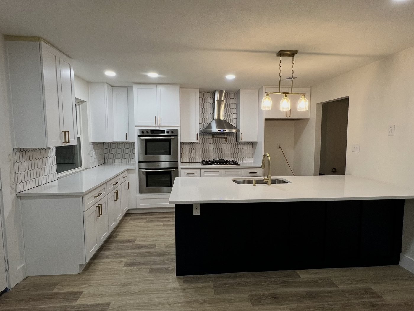 Remodeled kitchen with white shaker cabinets, black island, stainless hood and pendant lights