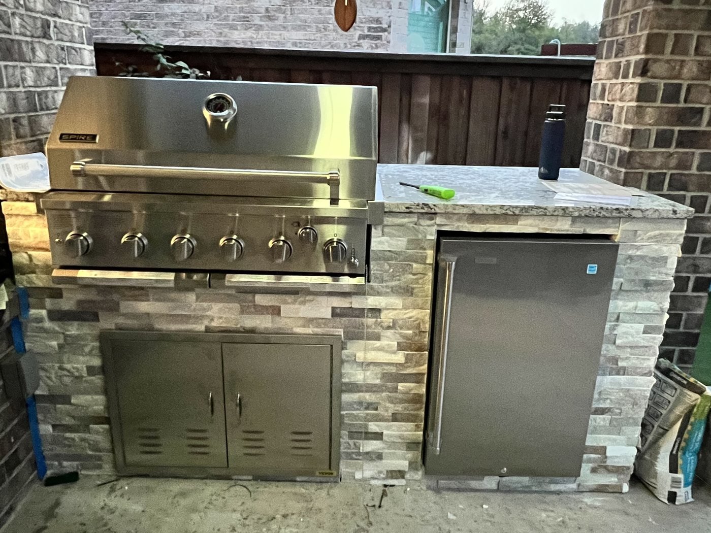 Backyard outdoor kitchen with built-in grill, beverage fridge, stone veneer and granite top